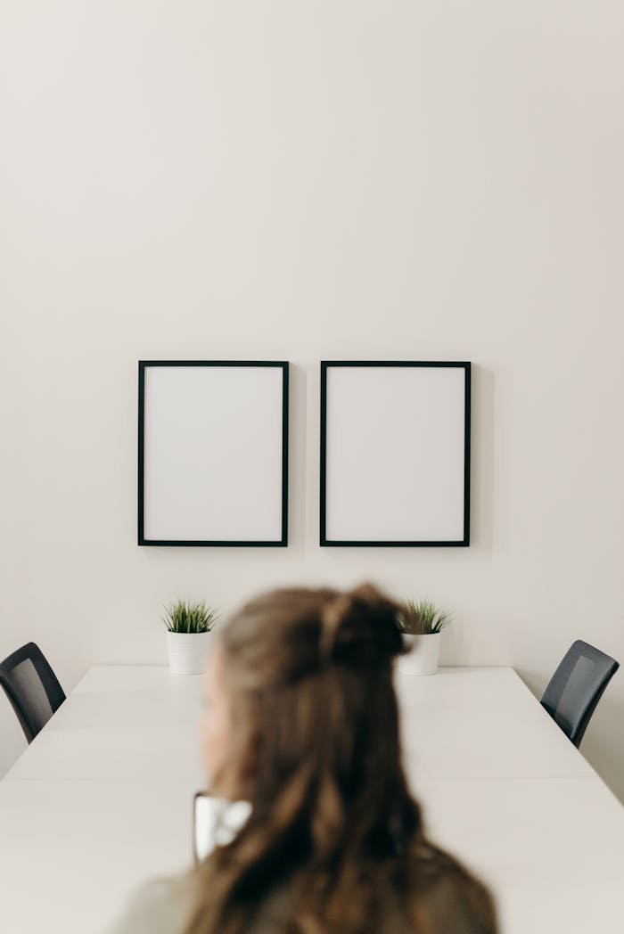 A minimalist workplace with blank frames on the wall and a person sitting at a table.